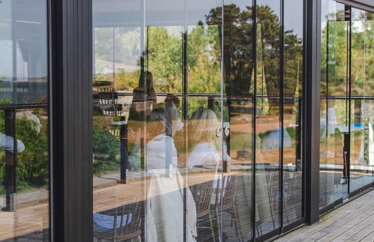 People in conversation inside a modern glass-walled conference room overlooking nature and a garden.