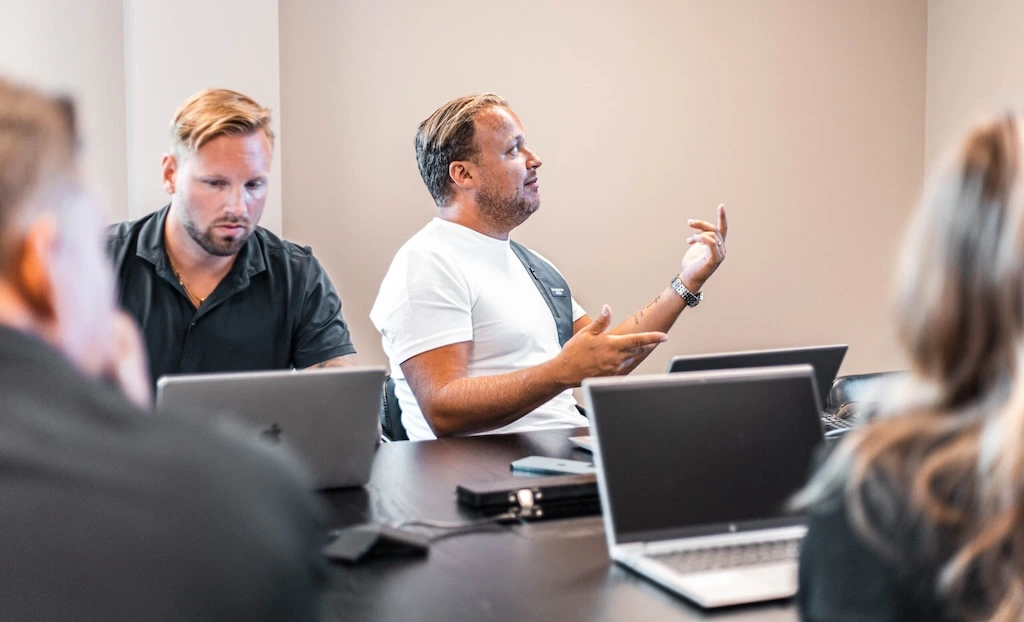 People at a conference table. One is speaking and gesturing while the other listens.